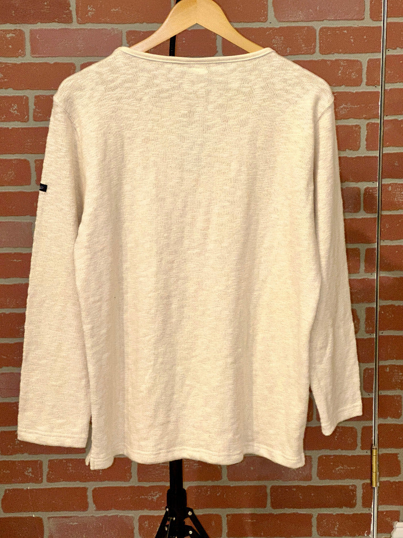 Beige long-sleeve shirt on a hanger against a brick wall.