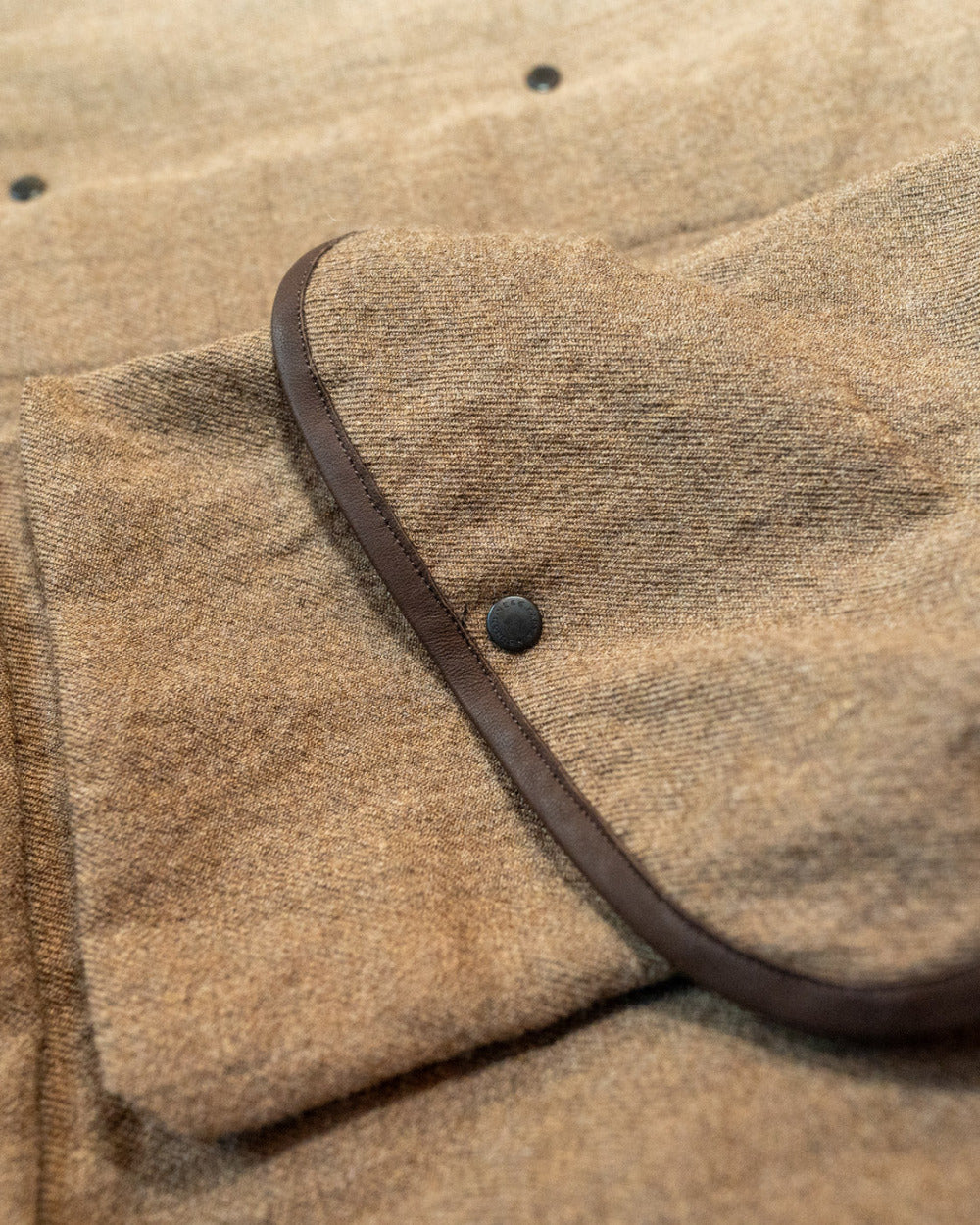 Close-up of a brown textured fabric with a leather strap and button.
