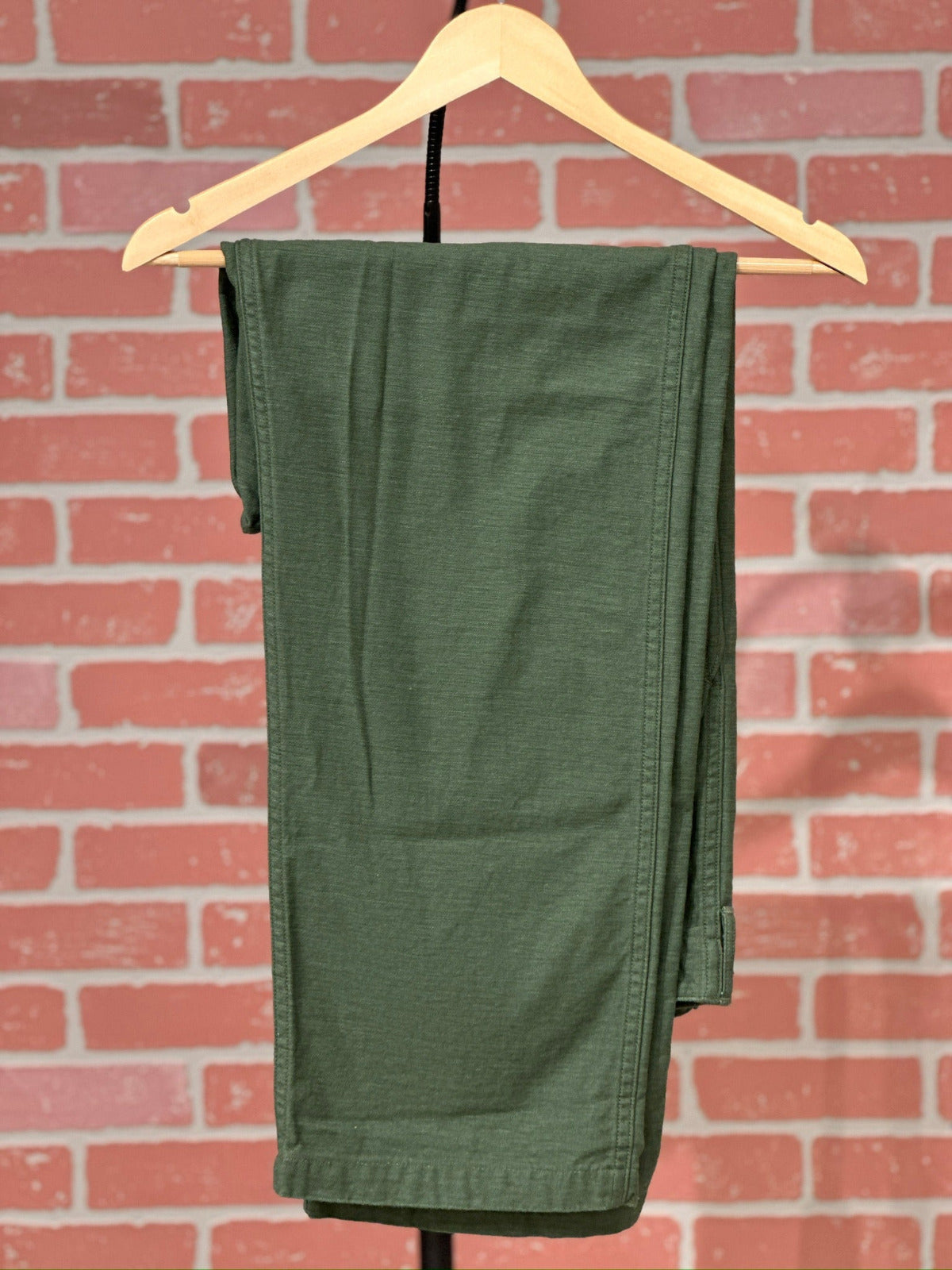 Green orslow pants on a hanger against a brick wall background