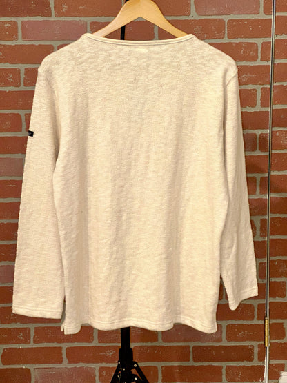 Beige long-sleeve shirt on a hanger against a brick wall.
