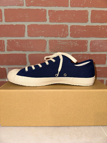 arch side view of Navy blue sneaker with white laces on a cardboard box against a brick wall.
