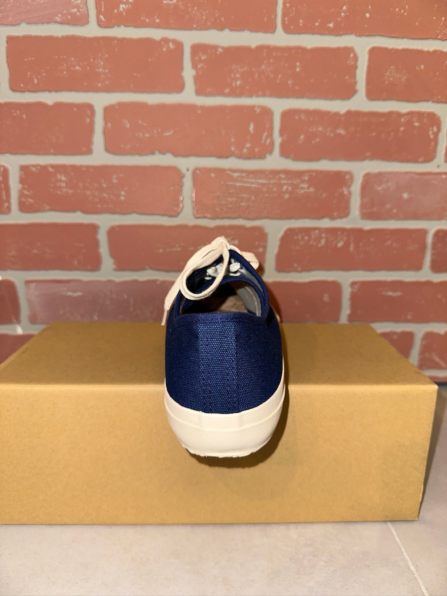Blue and white sneaker on a cardboard box with a brick wall background