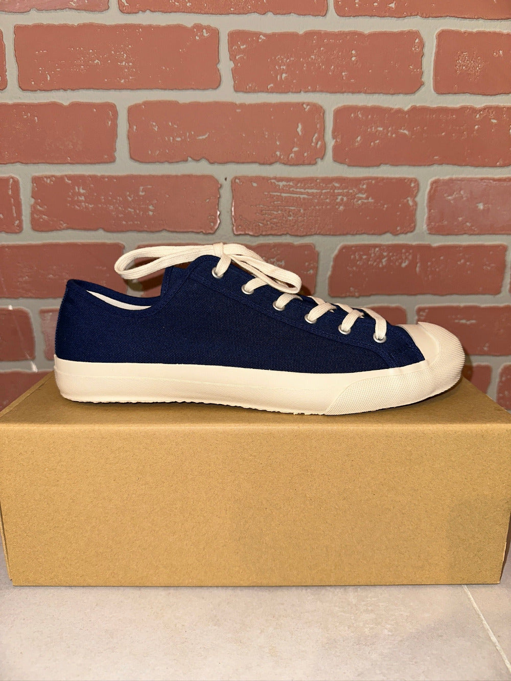 Blue sneaker with white laces on a cardboard box against a brick wall.
