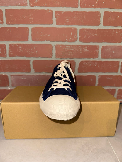 Navy and white sneaker on a cardboard box with a brick wall background