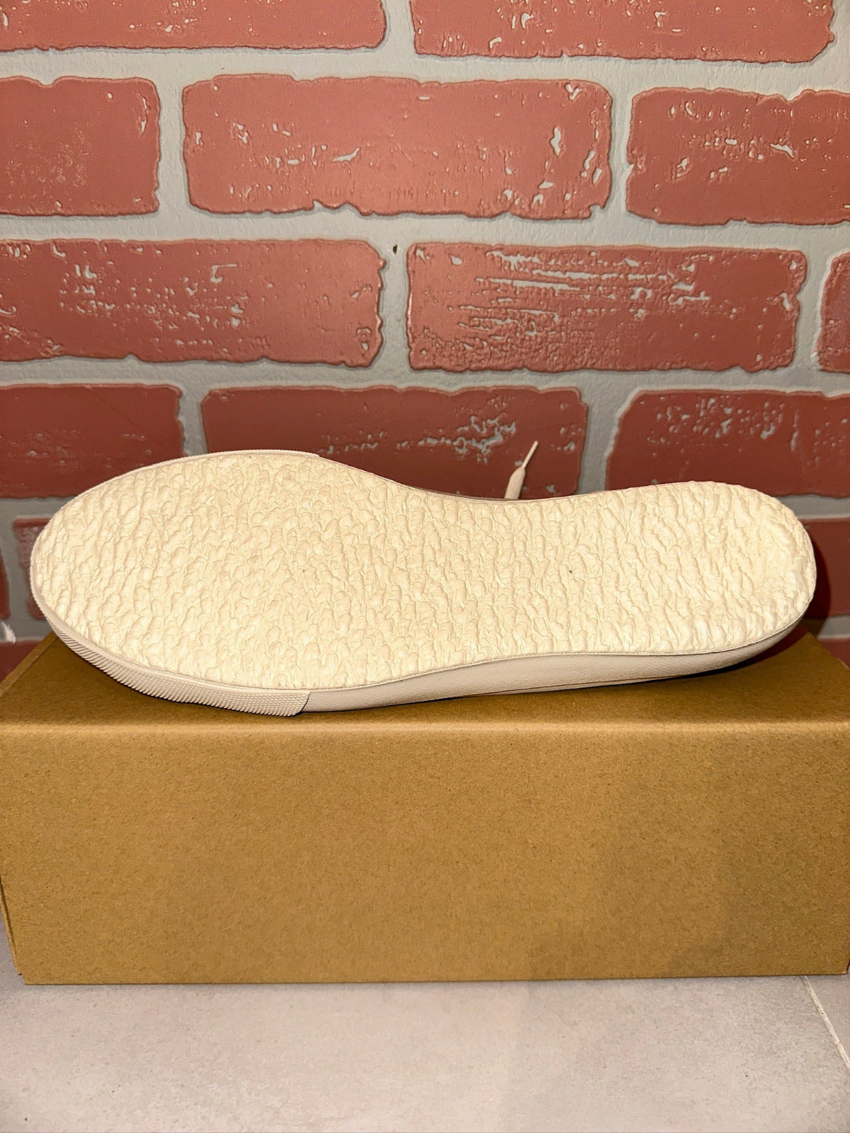 White shoe sole on a cardboard box with a brick wall background