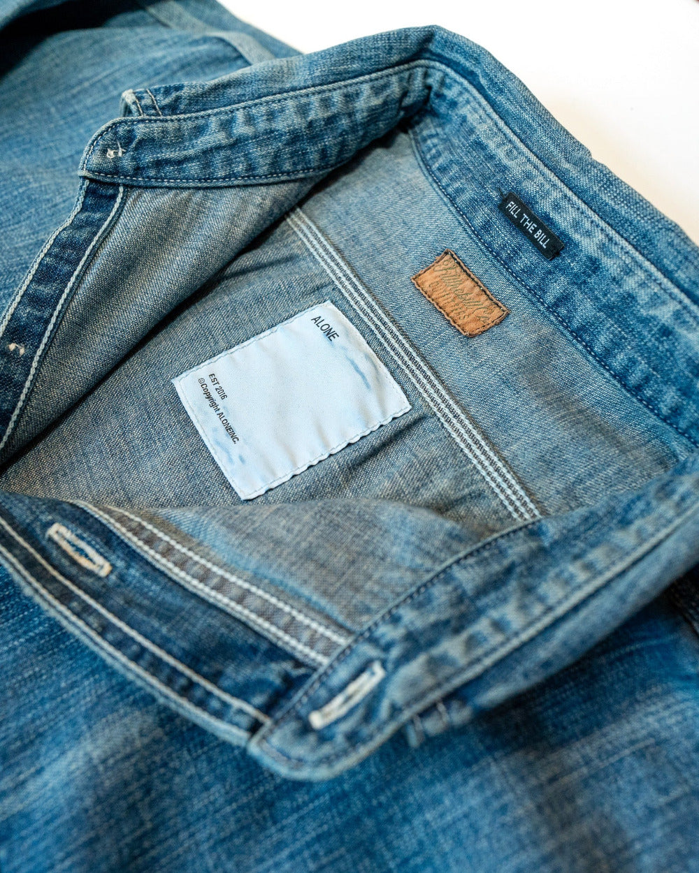 Close-up of blue denim shirt with a brand label on a white background