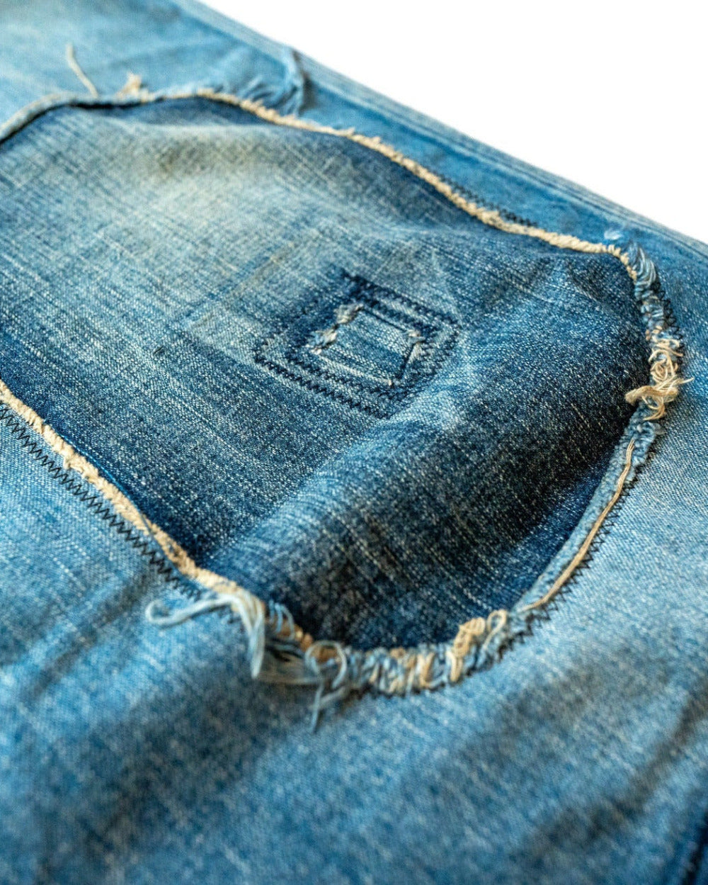 Close-up of a blue denim pants with a patch with frayed edges on a white background