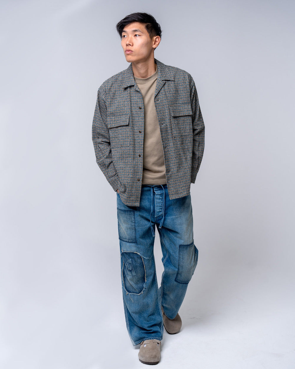 Man wearing a houndstooth shirt, beige shirt, and blue jeans on a white background