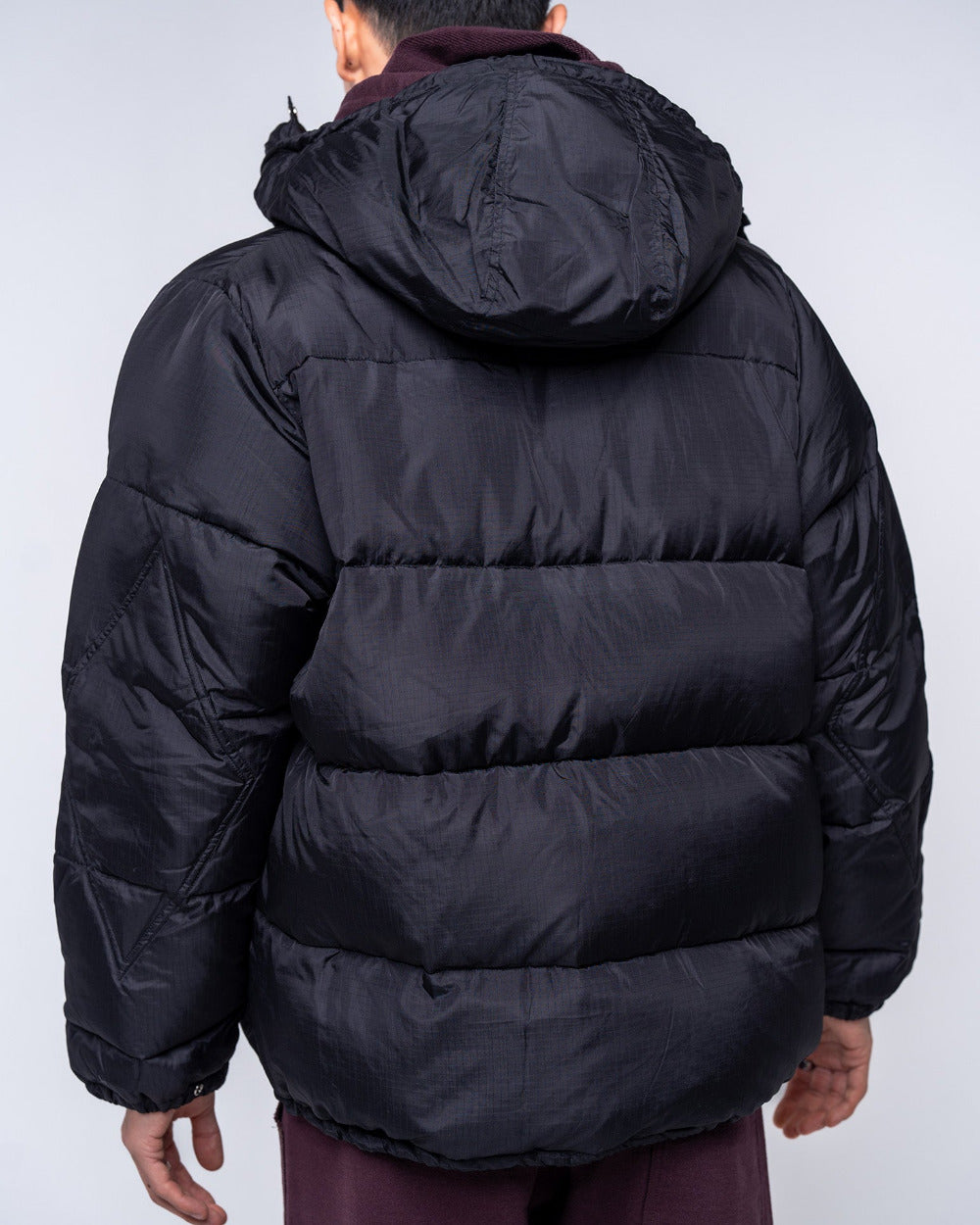 Black puffer jacket worn by a person on a light gray background