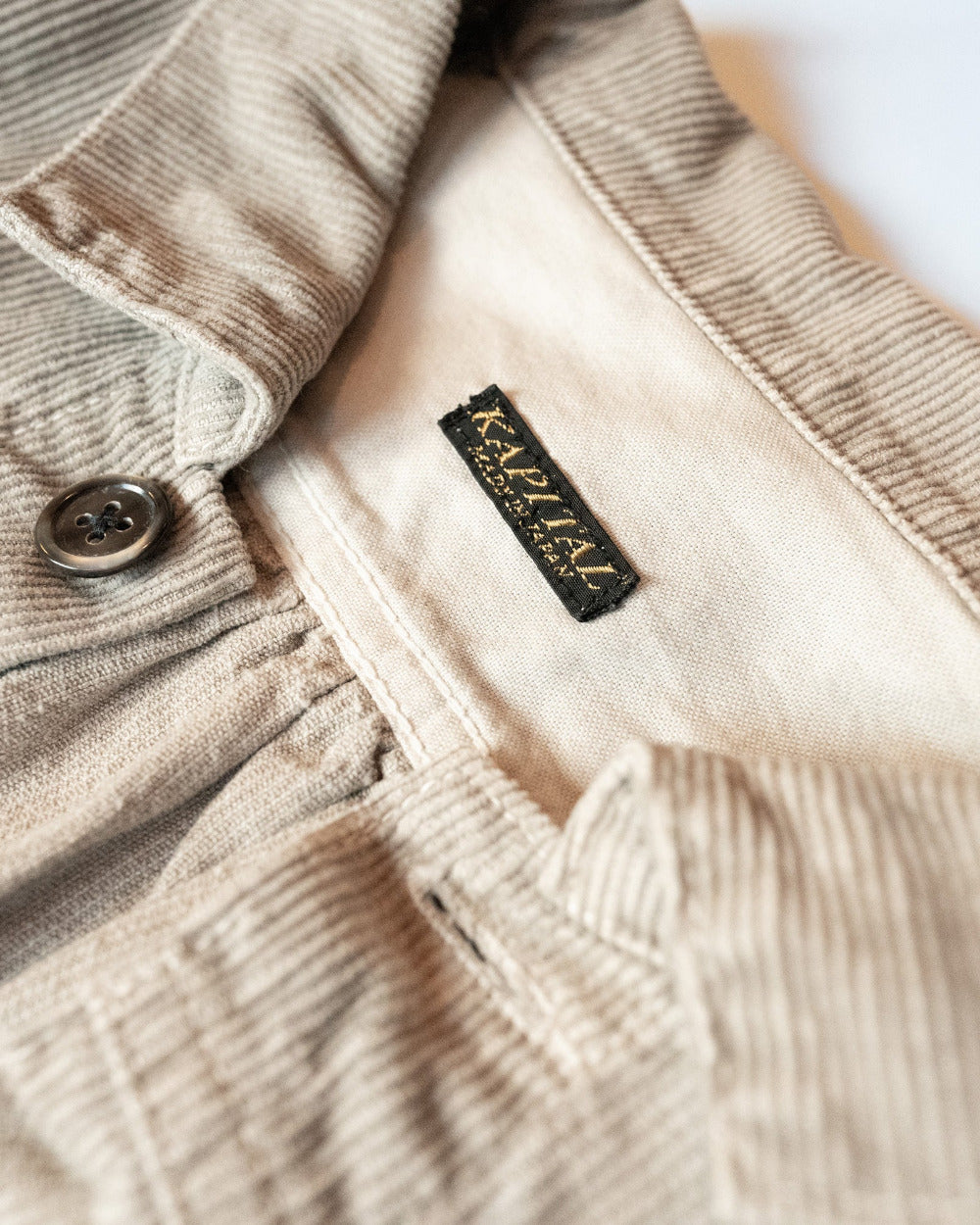 Close-up of a beige corduroy jacket with a kapital brand label on a white background