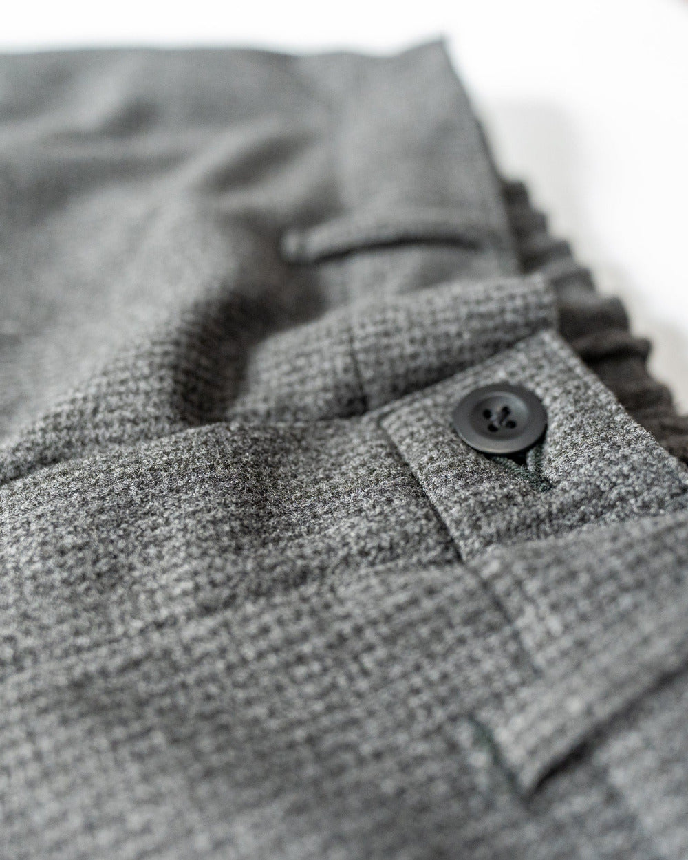 Close-up of gray textured fabric of a pair of pants' fly a button on a white background