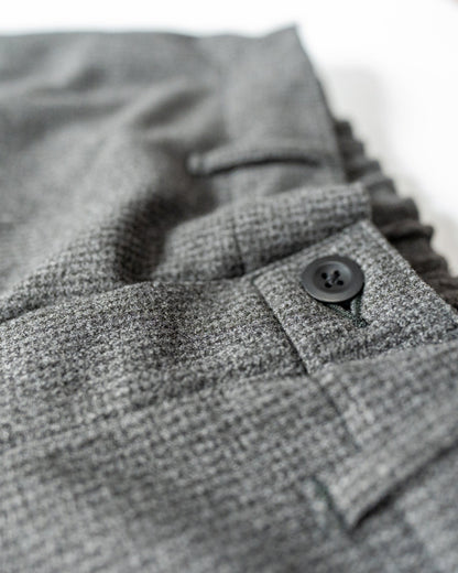 Close-up of gray textured fabric of a pair of pants' fly a button on a white background