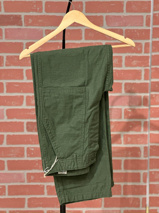 Green orslow fatigues on a hanger against a brick wall