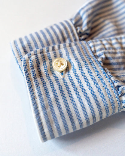 Close-up of a blue and white striped shirt cuff with a button on a light background