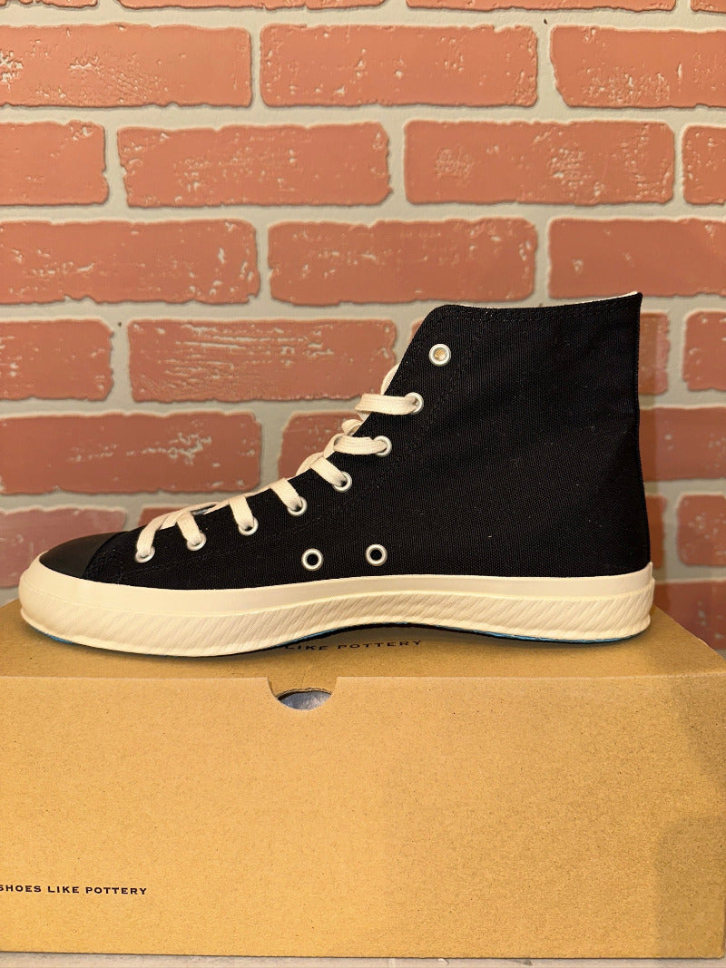 Black high-top sneaker on a cardboard box with a brick wall background