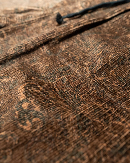 Close-up of a paisley textured brown fabric with a brand logo.