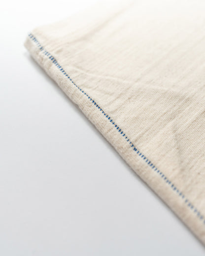 Close-up of a beige t-shirt with blue stitching pattern on a white background.