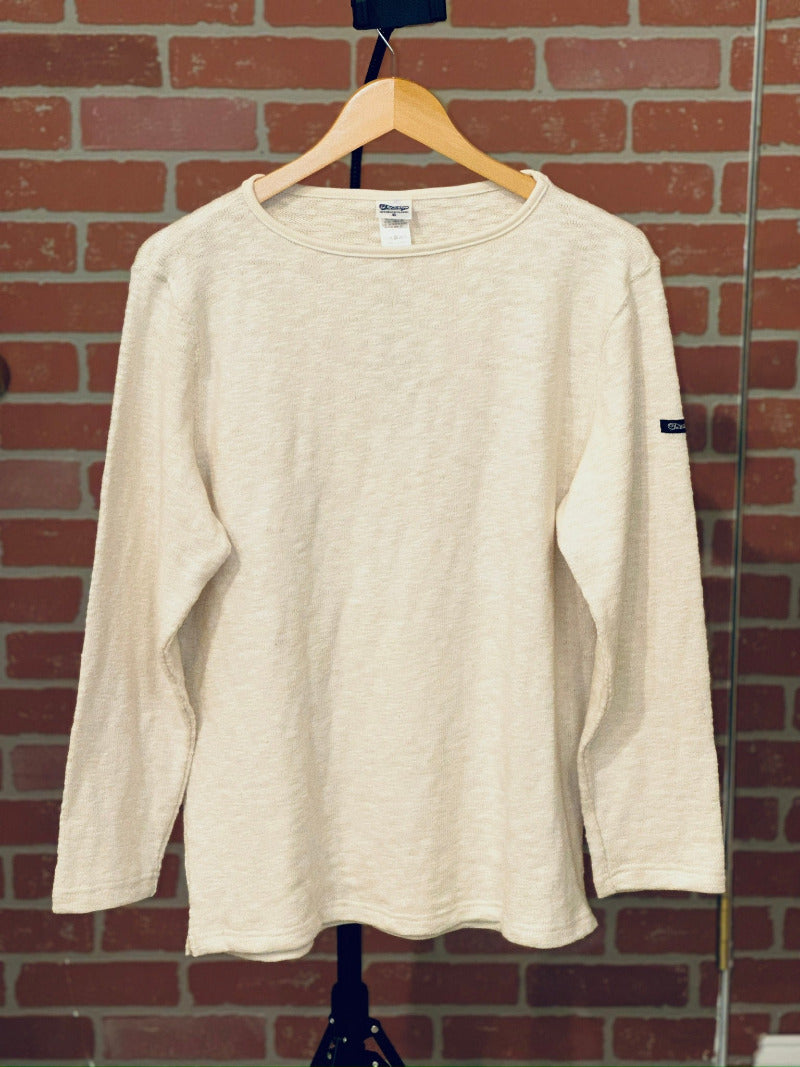 Beige long-sleeve shirt on a hanger against a brick wall