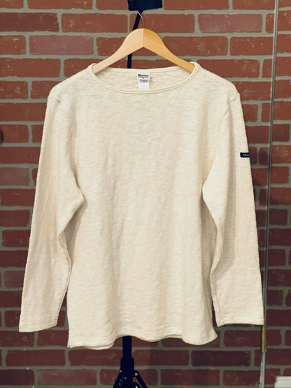 Beige long-sleeve shirt on a hanger against a brick wall